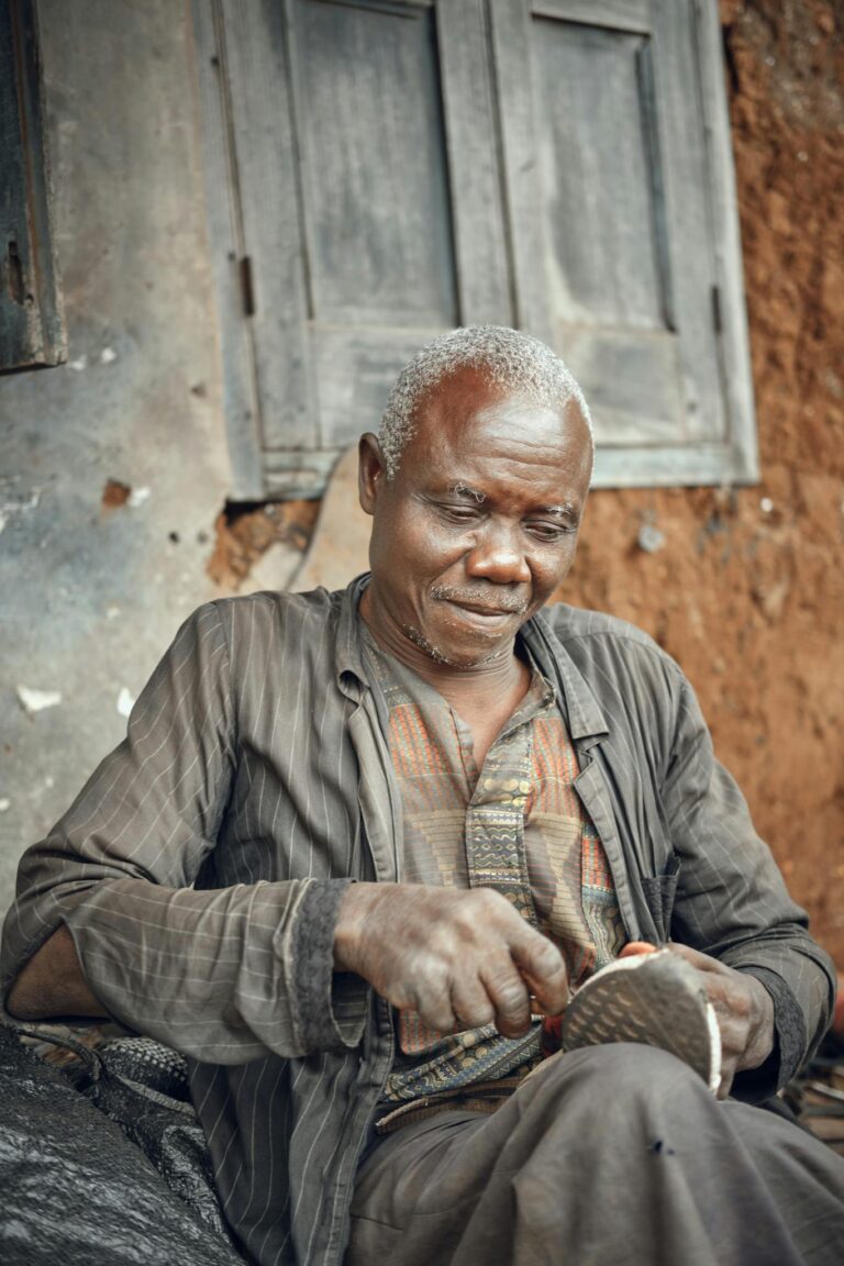 Senior shoemaker working on a shoe outdoors, showcasing traditional craftsmanship.